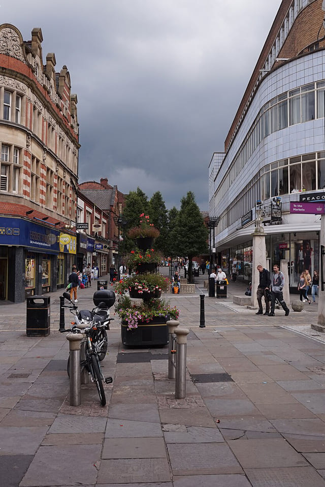 Doncaster town centre with a mix of traditional and modern buildings, shopfronts, and scattered pedestrians on a bright day with blue sky.