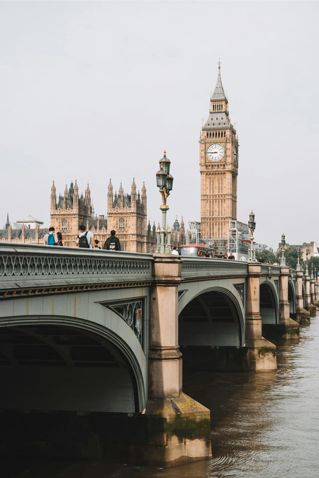 Westminster Bridge over the River Thames with people walking and traffic, leading towards the Elizabeth Tower and the Houses of Parliament at the heart of London.